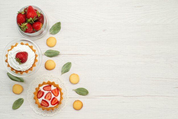 Top view of fresh red strawberries mellow and delicious berries with cakes and cookies on light desk, fruit berry red fresh