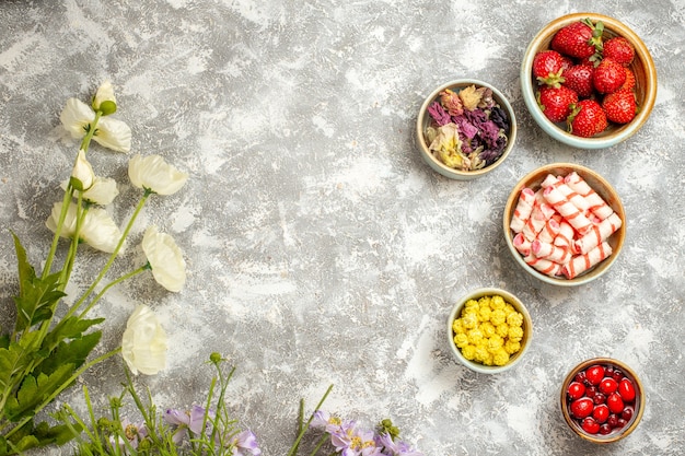 Foto gratuita vista dall'alto fragole rosse fresche con caramelle sul fiore di gelatina di frutta superficie bianca