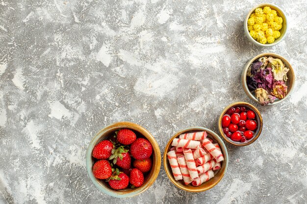 Вид сверху свежей красной клубники с конфетами на белой поверхности фруктовых сладких конфет