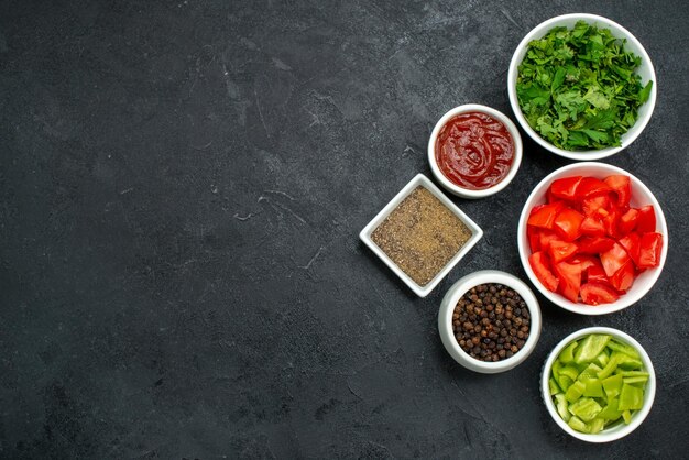 Top view of fresh red tomatoes sliced vegetables with greens on black table