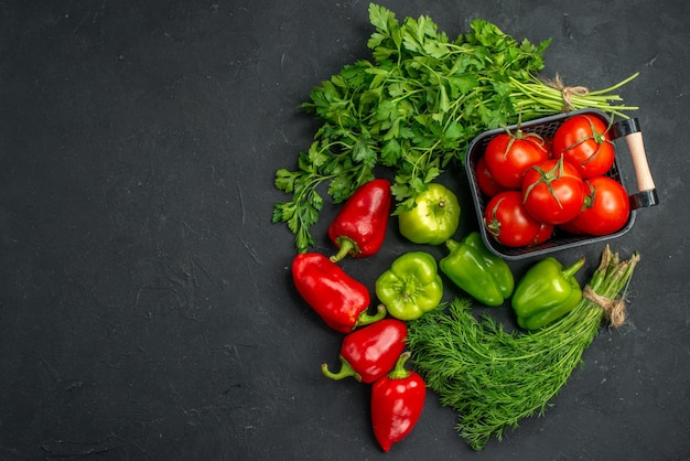 Top view fresh red tomatoes with greens and bell-peppers on dark background