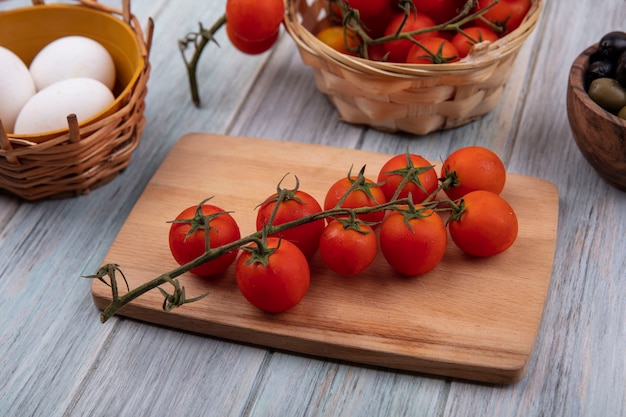 Vista dall'alto di pomodori rossi freschi su una tavola di cucina in legno con pomodori a grappolo su un secchio con uova biologiche e olive su un fondo di legno grigio