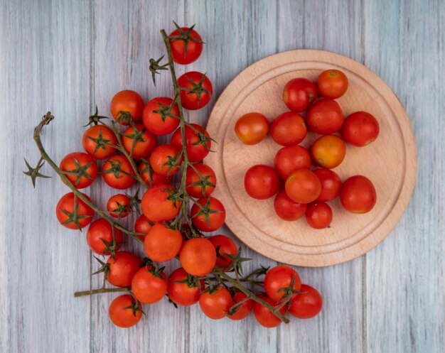 Вид сверху свежих красных виноградных помидоров на миске с помидорами, изолированными на деревянной кухонной доске на сером деревянном фоне