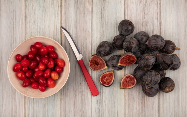 Top view of fresh ripe black mission figs with cornelian cherries on a bowl with knife on a grey wooden wall