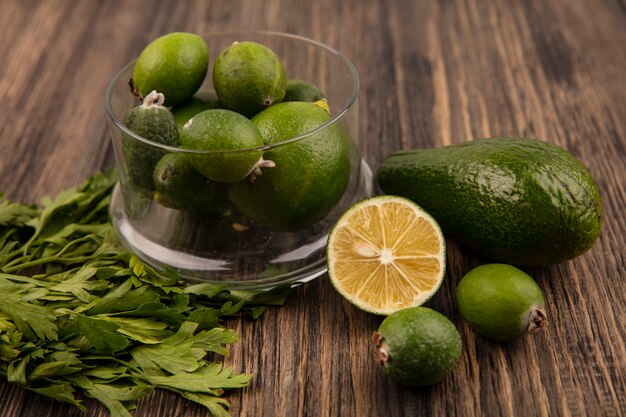 Top view of fresh ripe feijoas on a glass bowl with avocado half lime feijoas and parsley isolated on a wooden surface