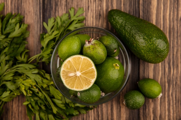 Top view of fresh ripe feijoas with limes on a glass bowl with avocado feijoas and parsley isolated on a wooden wall