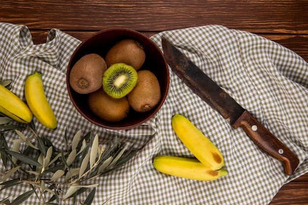 Top view of fresh ripe kiwi fruits in a wooden bowl and fresh bananas with old kitchen knife on rustic