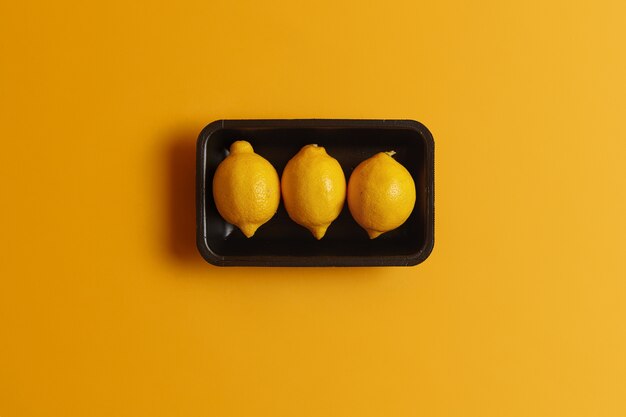 Свежие спелые лимоны в контейнере, вид сверху, можно украсить другими блюдами, чтобы придать им кислый вкус. Ключевой ингредиент для приготовления лимонада. Цитрусовые, содержащие витамины, минералы и эфирные масла