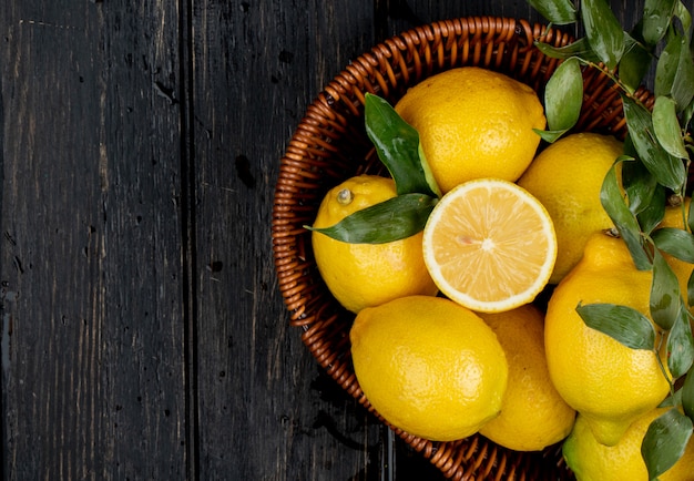 Top view of fresh ripe lemons in a wicker basket on black with copy space