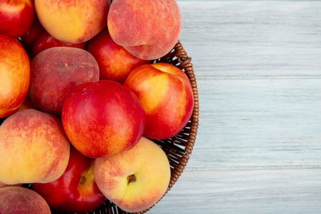 Top view of fresh ripe nectarines and peaches in a wicker basket on white background with copy space