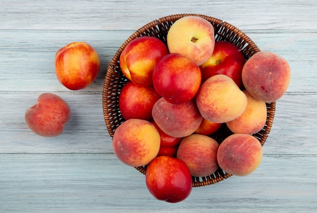 Top view of fresh ripe nectarines and peaches in a wicker basket on white background