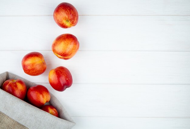 top view of fresh ripe nectarines scattered from a sack on white surface with copy space