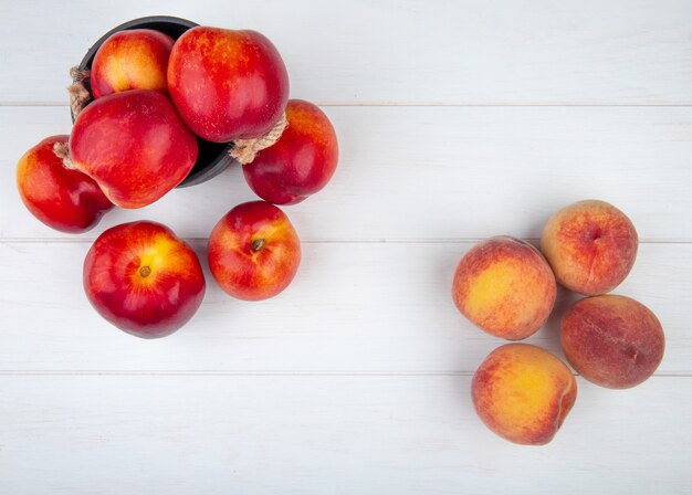 Top view of fresh ripe nectarines in a small bucket and fresh peaches on white