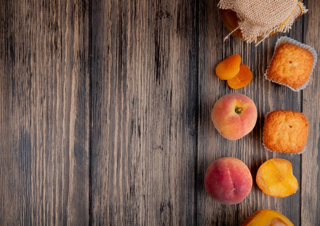 Free photo top view of fresh ripe peaches with muffins and peach jam in a glass jar on rustic wooden table with copy space