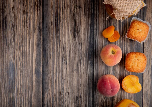 вид сверху свежих спелых персиков с кексами и персиковым джемом в стеклянной банке на деревенский деревянный стол с копией пространства