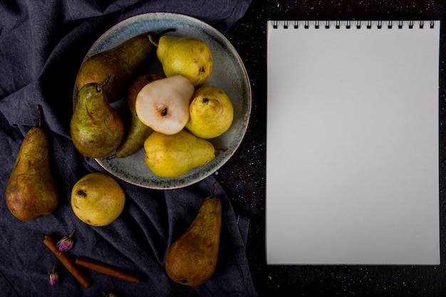 Top view of fresh ripe pears on a ceramic plate with sketchbook on black background with copy space