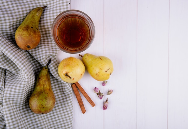 白い背景の格子縞のテーブルクロスに新鮮な熟した梨とシナモンスティックジュースのガラスのトップビュー