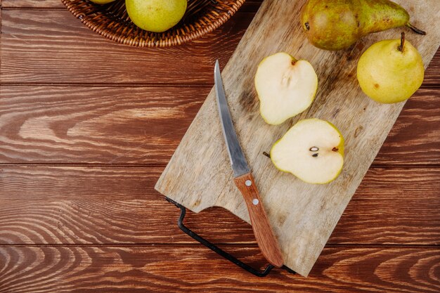 Top view of fresh ripe pears and halves on a wooden cutting board with kitchen knife on rustic background with copy space