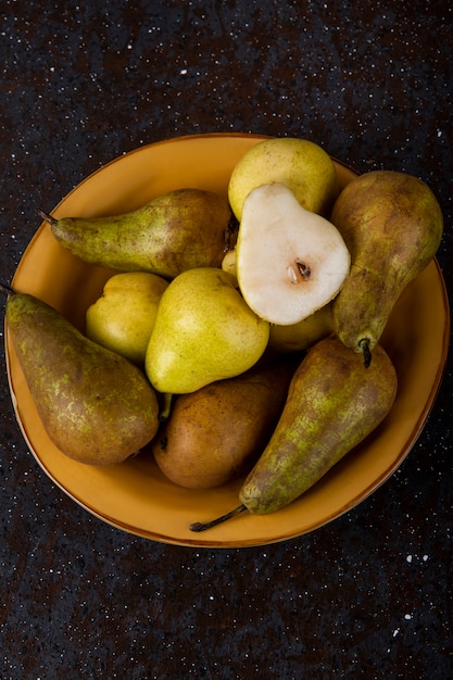 Top view of fresh ripe pears on a plate on black background