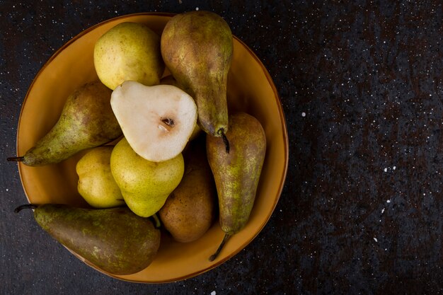 Top view of fresh ripe pears on a plate on black background