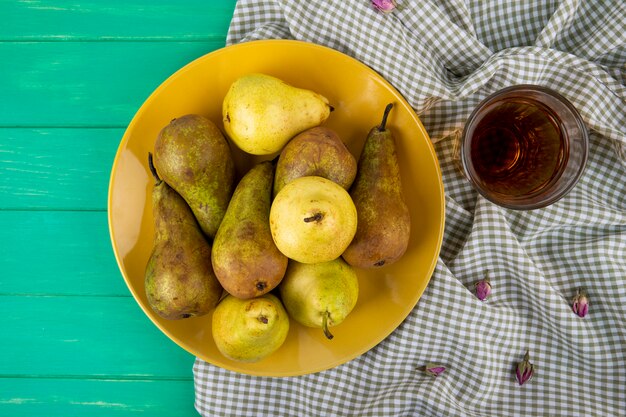 Top view of fresh ripe pears in a plate and a glass of juice on green wooden background