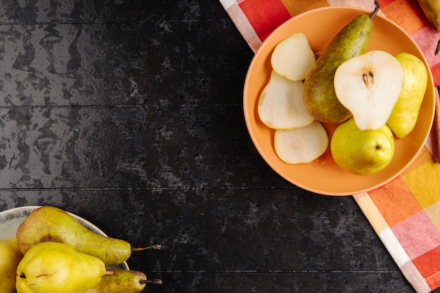 Top view of fresh ripe pears and slices of pears on a plate on black background with copy space