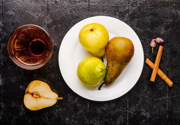 Top view of fresh ripe pears on a white plate and a glass of pear juice on black background