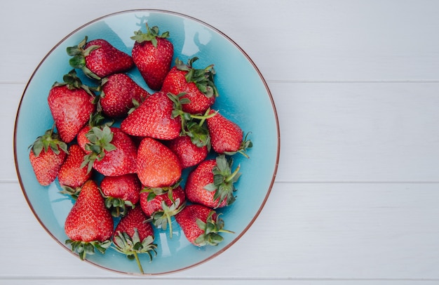 Free photo top view of fresh ripe strawberries on a blue plate on white with copy space