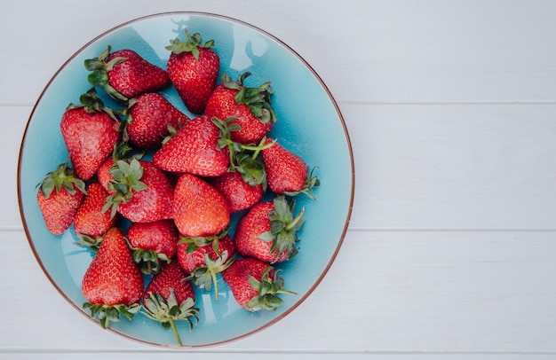 Top view of fresh ripe strawberries on a blue plate on white with copy space