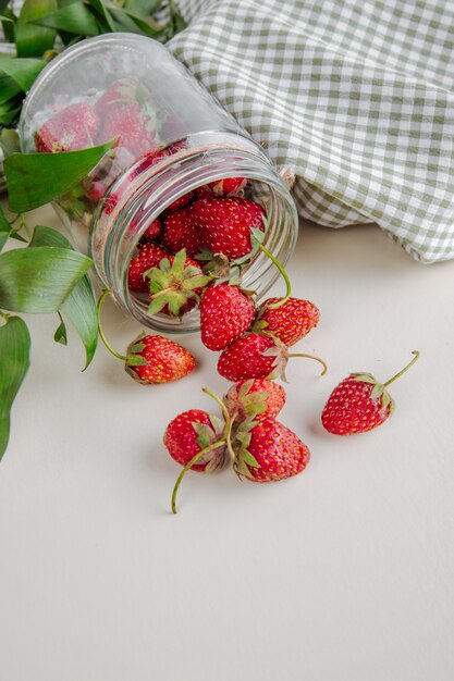 Top view of fresh ripe strawberries scattered from glass jar on white