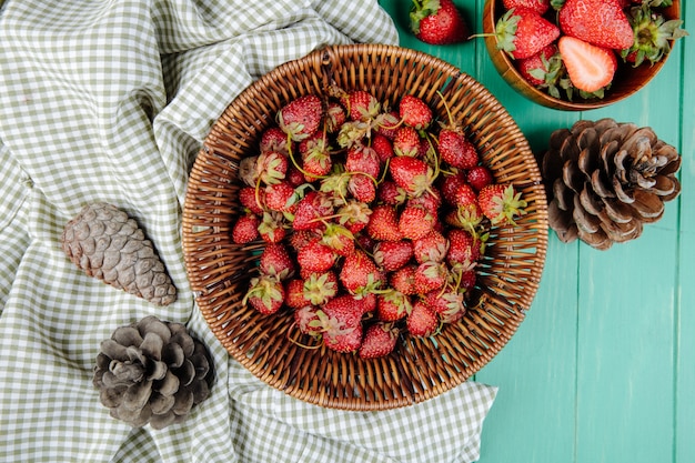 Top view of fresh ripe strawberries in a wicker basket and cones on green wood