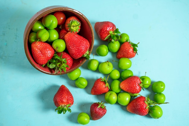 top view of fresh ripe strawberries with sour green plums on blue table