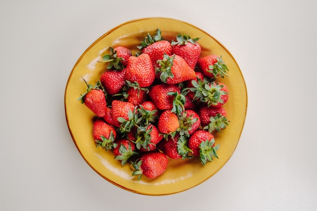 Top view of fresh ripe strawberries in a yellow plate on white