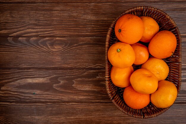 Top view of fresh ripe tangerines in a wicker basket on wood with copy space