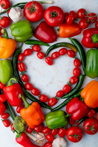 Free photo top view of fresh ripe vegetables arranged in a heart shape cherry tomatoes green chili pepper bell pepper garlic and onion on marble background