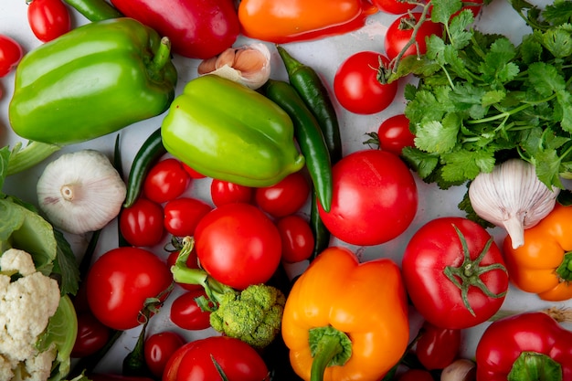 Вид сверху свежих спелых овощей, как помидоры, красочные сладкий перец, зеленый перец, чеснок, зеленый лук и брокколи на белом фоне