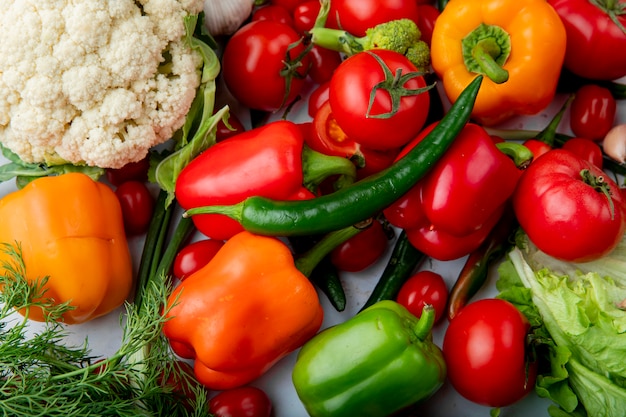 Top view of fresh ripe vegetables tomatoes green chili pepper colorful bell peppers garlic broccoli and cauliflower on marble background