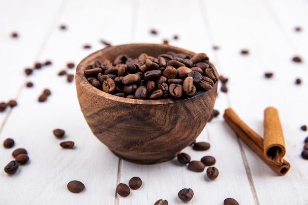 Top view of fresh roasted coffee beans on a wooden bowl with cinnamon sticks on a white background