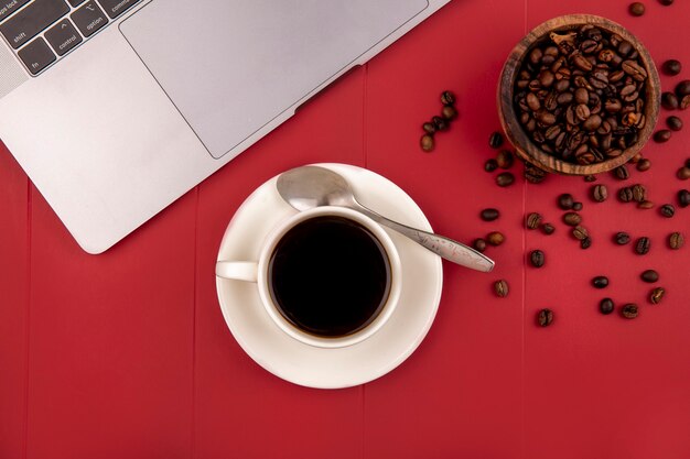 Top view of fresh roasted coffee beans on a wooden bowl with a cup of tea on a red background