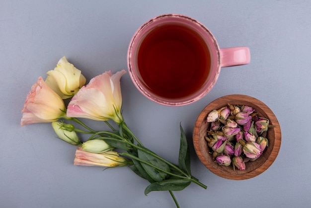 Free photo top view of fresh rose buds on a wooden bowl with a cup of tea on a gray background