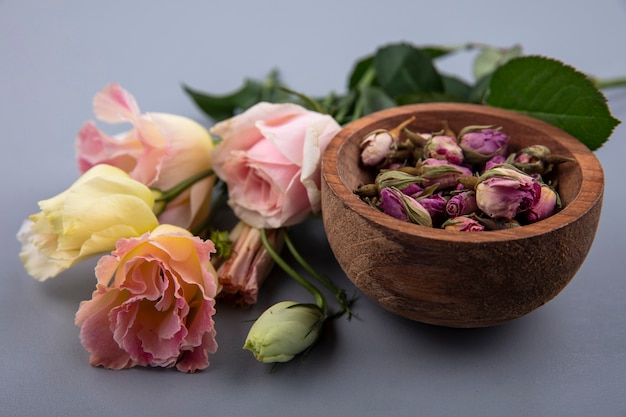 Top view of fresh rose buds on a wooden bowl with fresh leaves on a gray background