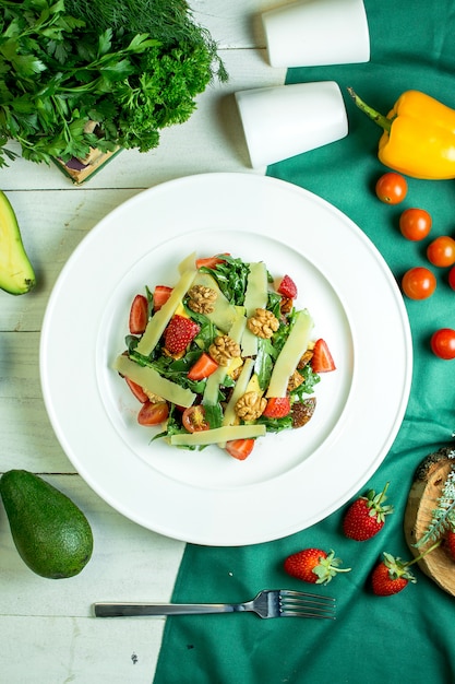 Vista dall'alto di insalata fresca con parmigiano noci pomodori ciliegia e fragole in una ciotola bianca