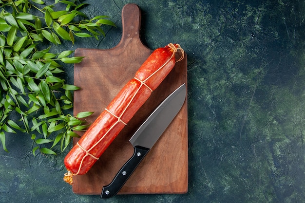 Top view fresh sausage with knife and green leaves on dark-blue background bread bun meat burger animal color meal sandwich food