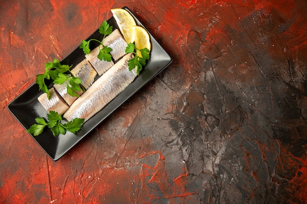 Free photo top view fresh sliced fish with greens and lemon pieces inside black pan on dark background