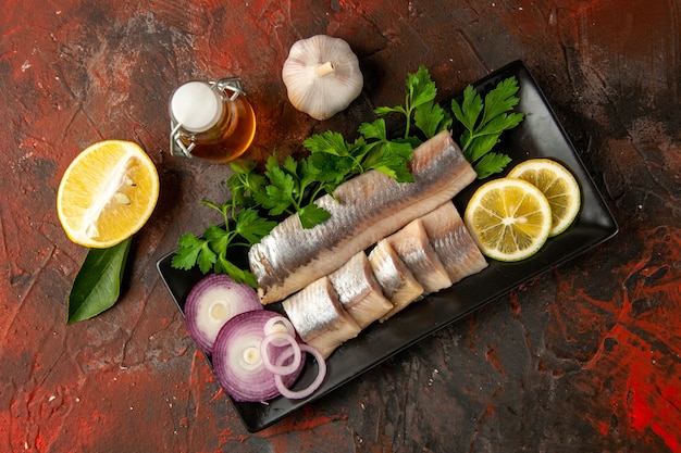 Top view fresh sliced fish with greens and onion inside black pan on dark background