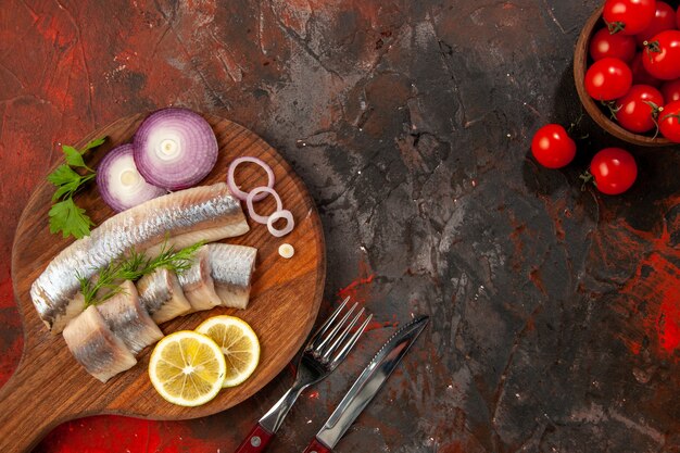 暗い背景にオニオンリングとフレッシュトマトを添えた新鮮なスライス魚の上面図