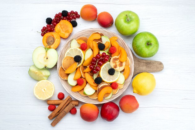Foto gratuita una vista dall'alto frutta fresca affettata colorata e matura con frutti interi e cannella sullo scrittorio di legno e sfondo bianco frutta a colori foto di cibo