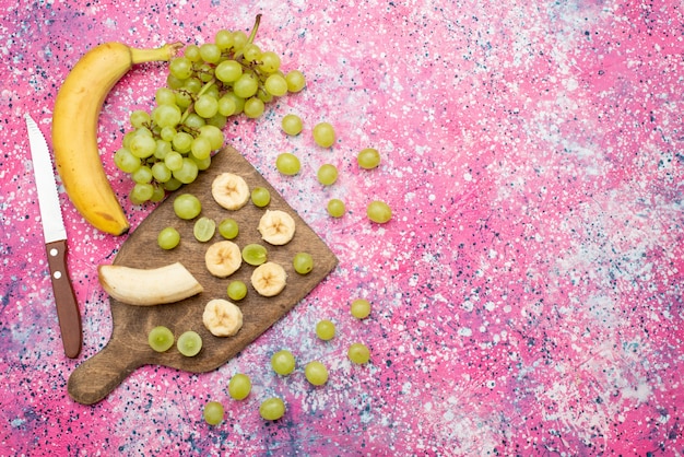 Вид сверху свежие нарезанные фрукты свежий виноград и бананы на фиолетовой поверхности цвет фруктового сока