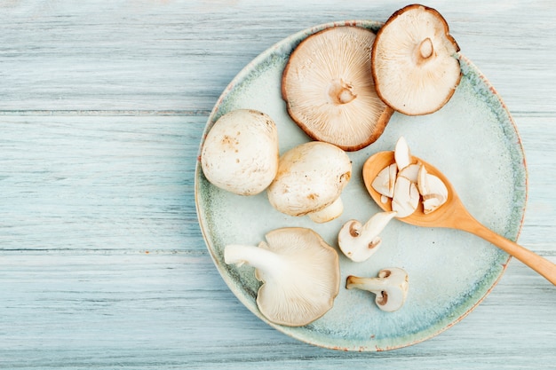 Free photo top view of fresh sliced mushrooms in a wooden spoon on a plate with whole mushrooms on rustic wooden table with copy space