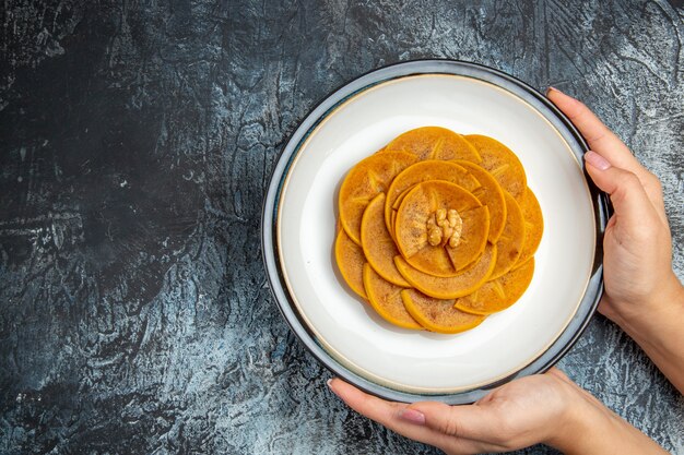 Top view of fresh sliced persimmons inside plate on dark surface